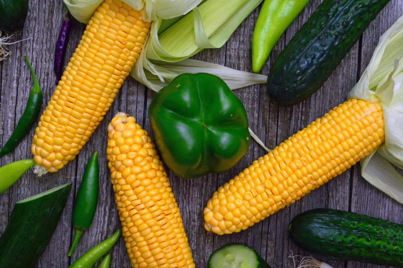 Vibrant arrangement of corn, cucumber, and peppers on a wooden table, ideal for healthy cooking and organic farming themes.